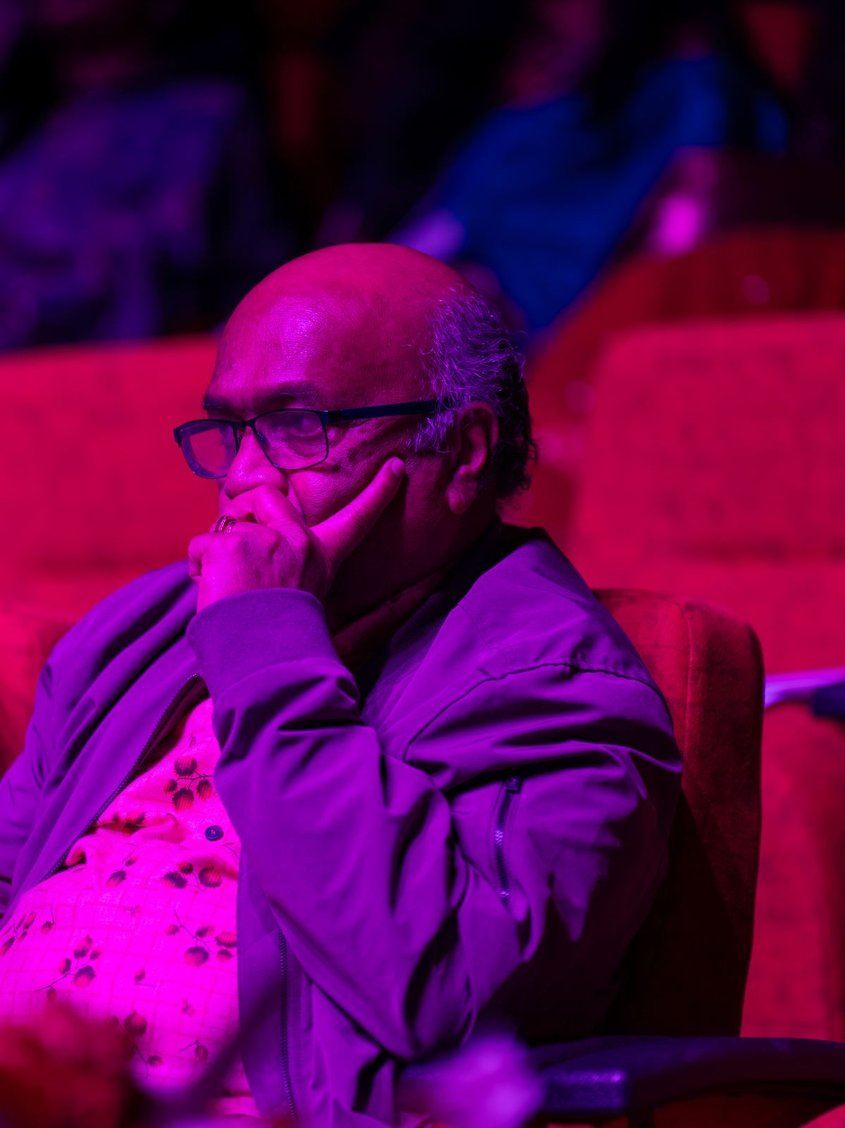 An audience member listening, lit in magenta