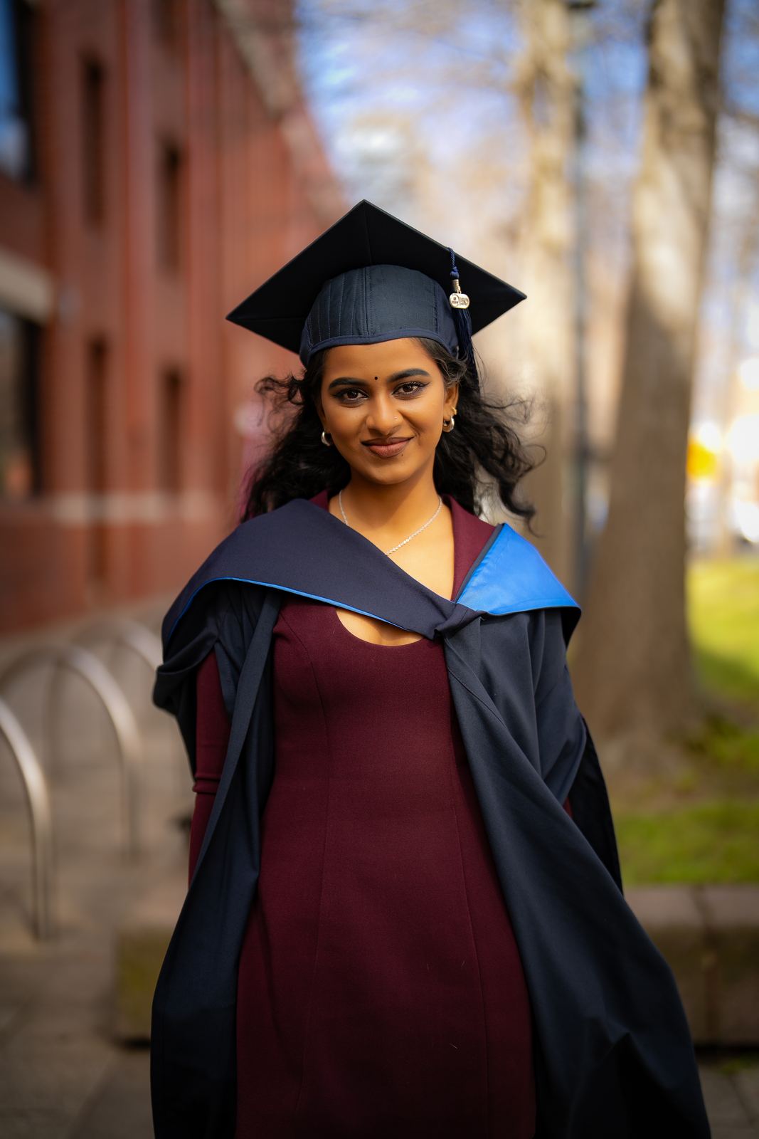 Graduate in cap and gown on a leafy campus street