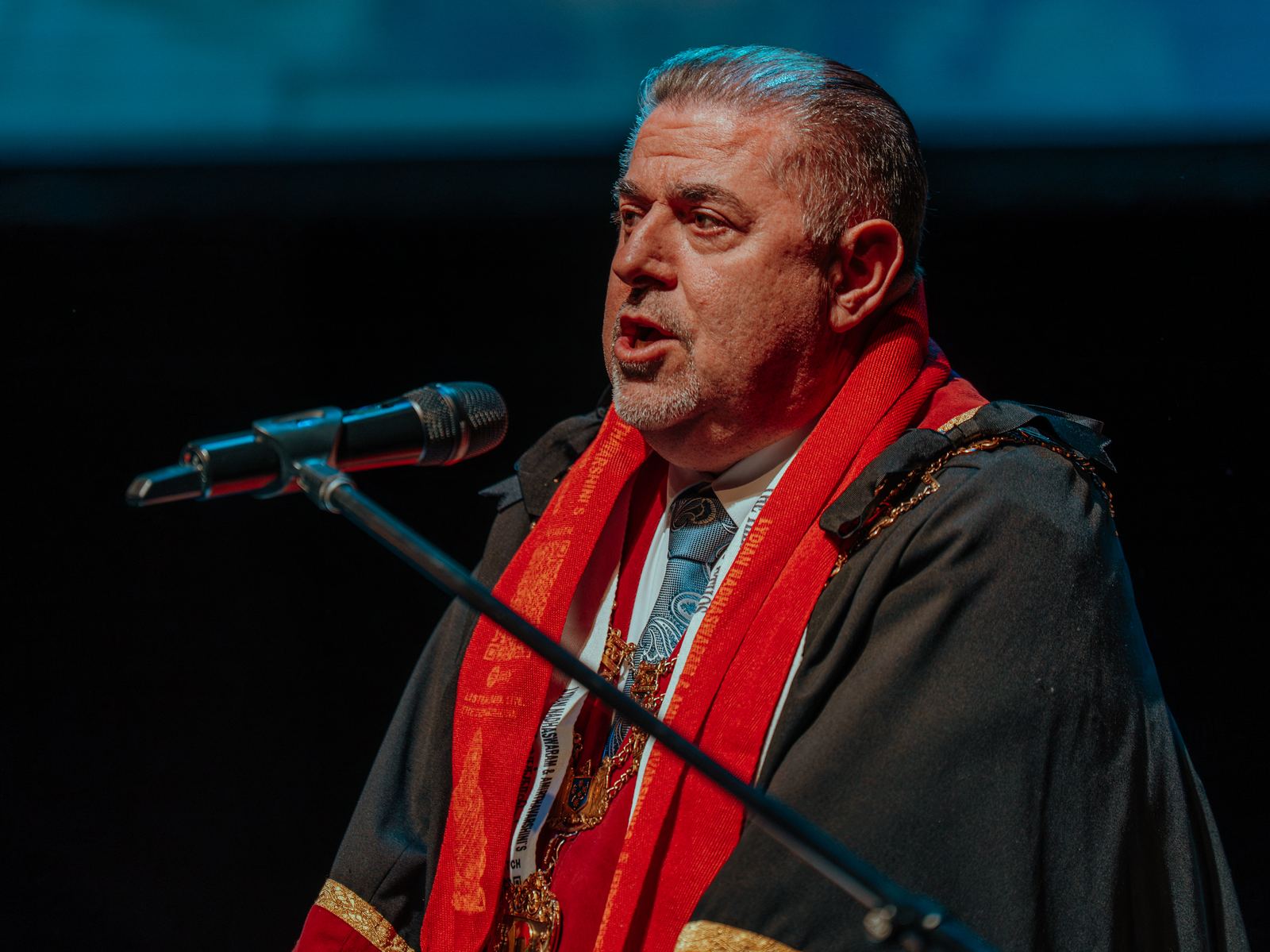 A civic guest in ceremonial robes speaking