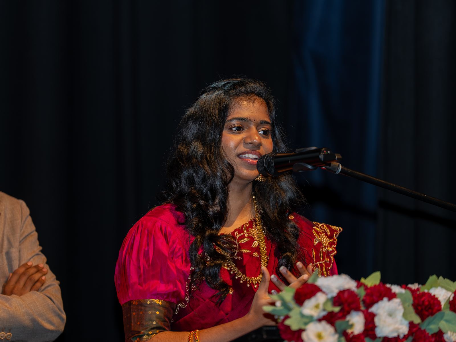 A presenter in a red saree at the microphone